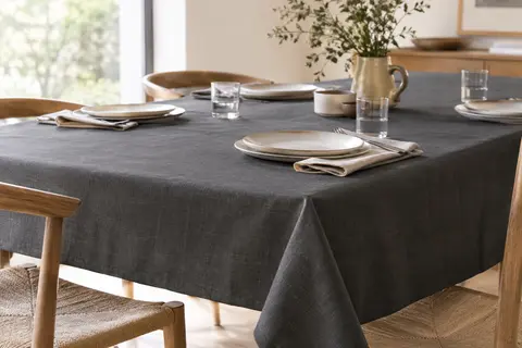 Nappe rectangulaire gris foncé à l’aspect lin disposée sur une grande table en bois clair.