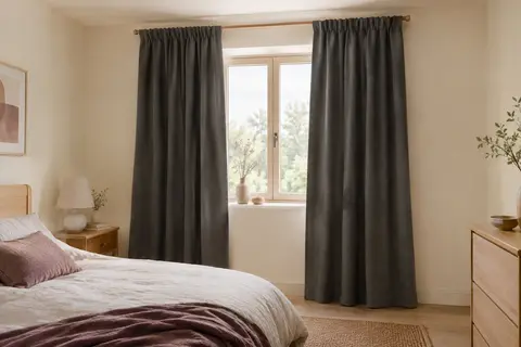 Deux rideaux occultants gris foncé en polyester habillent une petite fenêtre dans une chambre lumineuse.