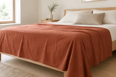 Drap plat uni en coton paprika disposé sur un lit dans une chambre lumineuse aux tons doux.