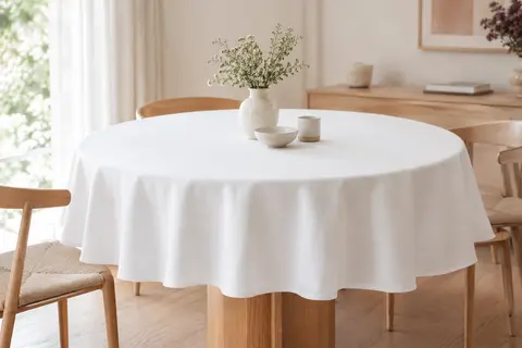 Nappe ronde blanche en polyester posée sur une table en bois clair dans une salle à manger lumineuse.