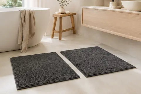 Deux tapis de bain rectangulaires en coton éponge gris anthracite posés sur un sol clair