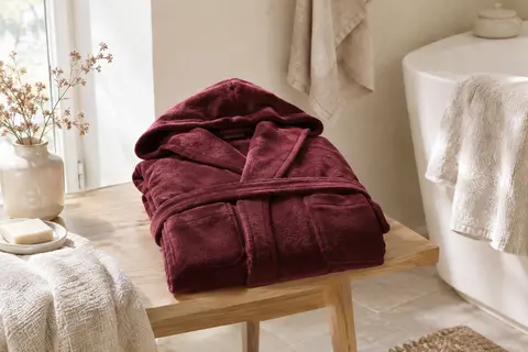 Peignoir long bordeaux en flanelle avec capuche et poches, posé dans une salle de bain lumineuse.