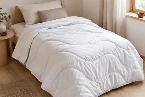 Couette blanche légère en microfibre avec matelassage ondulé, posée sur un lit dans une chambre claire.