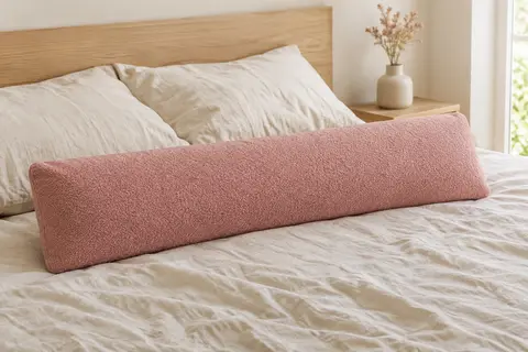Traversin rectangulaire rose posé sur un lit clair dans une chambre lumineuse aux matières naturelles.