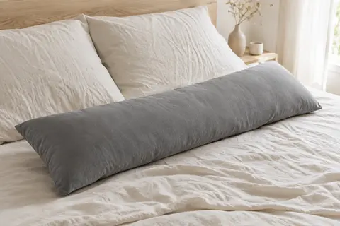 Oreiller de corps rectangulaire gris en polyester posé sur un lit aux draps crème