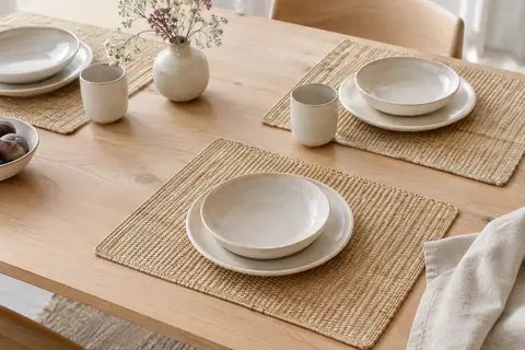 Quatre sets de table rectangulaires tressés en fibres naturelles posés sur une table en bois clair.